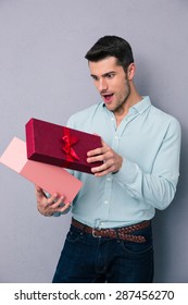 Happy Young Man Opening Gift Box Over Gray Backgorund