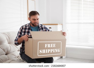 Happy Young Man Opening Parcel At Home. Free Shipping