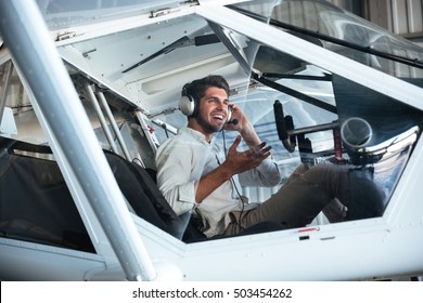 Happy Young Man Pilot Sitting In Small Plane And Talking Using Headset