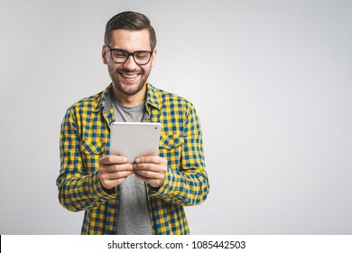 Happy young man in plaid shirt standing and using tablet over grey background - Powered by Shutterstock