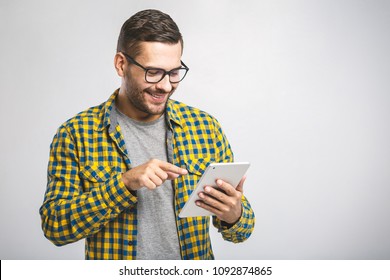 Happy young man in plaid shirt standing and using tablet over grey background - Powered by Shutterstock