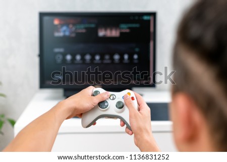 Happy young man playing and winning online game on computer. Back view of gamer with video console gamepad controller. Competitive gaming, electronic sports, technology, gaming, entertainment concept.