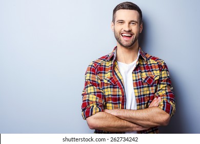 Happy young man. Portrait of handsome young man in casual shirt keeping arms crossed and smiling while standing against grey background - Shutterstock ID 262734242