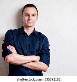 Happy young man. Portrait of handsome young man in casual shirt keeping arms crossed and smiling while standing against grey background
