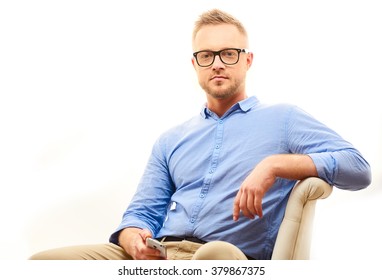 Happy Young Man. Portrait Of Handsome Young Man In Casual Blue Shirt And Dioptrical Glasses Sitting In Comfortable Pose Isolated On White Background