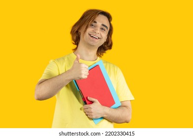 Happy Young Man Prep Student With Long Hair. Portrait Of A Guy With Thumbs Up On A Yellow Background.