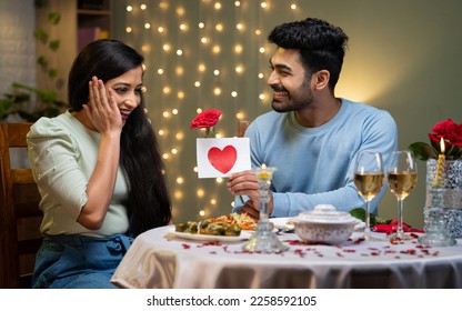 Happy young man proposing excited girl with rose and greetings during candle light dinner - concept of weedding anniversary, valentine's day celebration and romantic night - Powered by Shutterstock