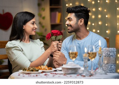 Happy young man proposing girl by giving red roses by arranging candle light dinner - concept of love emotions, wedding present and affectionate - Shutterstock ID 2259312873