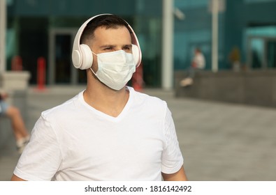 Happy Young Man In Protective Medical Face Mask Listen Music With Wireless Bluetooth Earphones. COVID-19 Coronavirus.