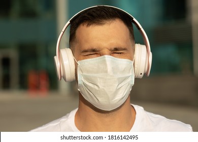 Happy Young Man In Protective Medical Face Mask Listen Music With Wireless Bluetooth Earphones. COVID-19 Coronavirus.