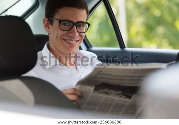 Happy young\
man reading newspaper in car,\
smiling.