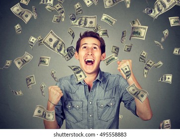 Happy young man screaming super excited. Portrait ecstatic guy celebrates success under money rain falling down dollar bills banknotes isolated gray background. Financial freedom concept