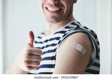 Happy young man showing thumb up and his arm after vaccination. Themes prevention, vaccine and health care during pandemic covid-19.