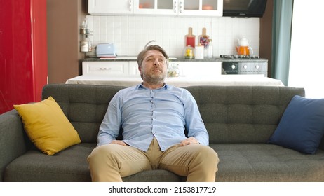 Happy Young Man Sitting Alone On Sofa At Home. Concept Of Happy Male At Home.Thoughtful Serious Young Man Alone Sitting Alone On Sofa At Home. Bored And Pensive Male Alone At Home Looking At Camera. 