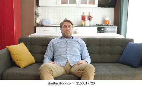 Happy young man sitting alone on sofa at home. Concept of happy male at home.Thoughtful serious young man alone sitting alone on sofa at home. Bored and pensive male alone at home looking at camera.  - Shutterstock ID 2153817723