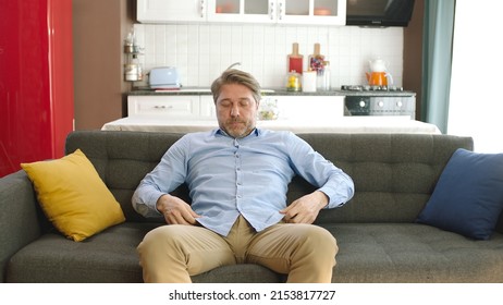 Happy Young Man Sitting Alone On Sofa At Home. Concept Of Happy Male At Home.Thoughtful Serious Young Man Alone Sitting Alone On Sofa At Home. Bored And Pensive Male Alone At Home Looking At Camera. 