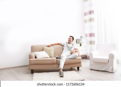 Happy young man sitting under air conditioner at home