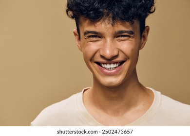 Happy young man smiling against a beige background, showcasing joy and positivity with natural lighting, capturing a moment of genuine happiness and warmth in a simple setting - Powered by Shutterstock