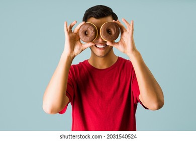 Happy young man smiling while holding two chocolate donuts in front of his eyes and having fun