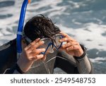 Happy young man spends time actively on vacation, swims in a wetsuit with equipment, puts a mask on his head and prepares for diving, swimming, snorkeling in the ocean.