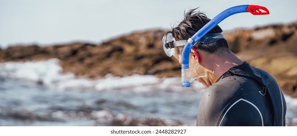 Happy young man spends time actively on vacation, swims in a wetsuit with equipment, puts a mask on his head and prepares for diving, swimming, snorkeling in the ocean.