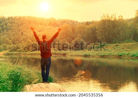 Happy young man standing alone with raised arms during a beautiful sunrise in the morning. The traveler is happy to be in nature. Enjoying nature. Copy space
