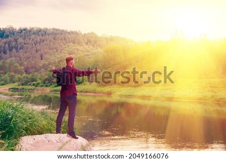 Happy young man standing alone with raised arms in the sun. Enjoying nature. The traveler is happy to be in nature. Copy space
