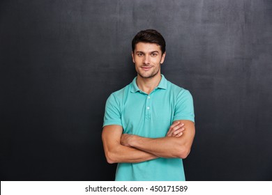 Happy Young Man Standing With Arms Crossed Over Blackboard Background