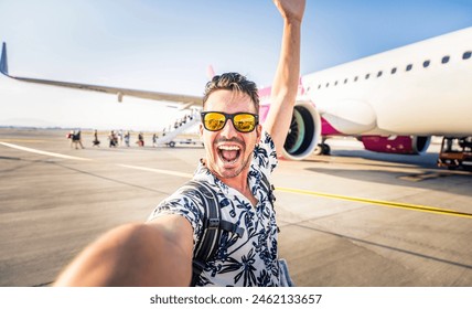 Happy young man taking selfie picture with smart mobile phone in front of airplane - Cheerful tourist standing at the airport - Travel life style concept with smiling guy going on summer vacation - Powered by Shutterstock