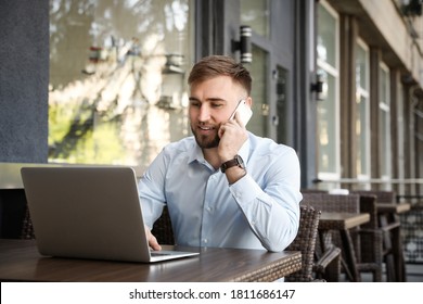 Happy young man talking on phone while using laptop at outdoor cafe - Powered by Shutterstock