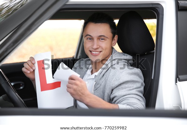 Happy young
man tearing learner driver sign in
car
