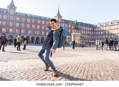 Happy Young Man Traveling Around Europe Having Fun Pretending To Surf In Plaza De Espa–a, Madrid, Spain. In People Vacations, Adventure, Backpacking, Student Lifestyle And Surfing The World Concept.