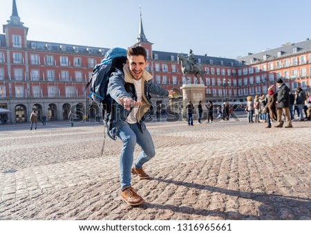 Happy young man traveling around Europe having fun pretending to surf in Plaza de Espa–a, Madrid, Spain. In People Vacations, adventure, backpacking, student lifestyle and surfing the world concept.