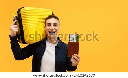 Happy young man travelling abroad, holding yellow suitcase and passport with flight tickets board pass, isolated on yellow studio background. Tourism, vacation, hot offer travelling deal, banner