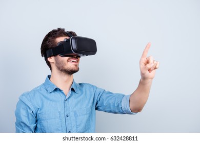Happy young man is using vh headset glasses of virtual reality, pointing on sopmething with finger