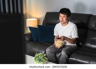 Happy Young Man Watching TV On Sofa At Night