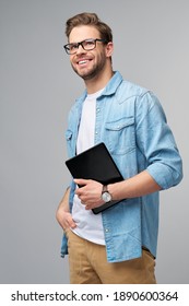 Happy young man wearing jeans shirt standing and using tablet over studio grey background