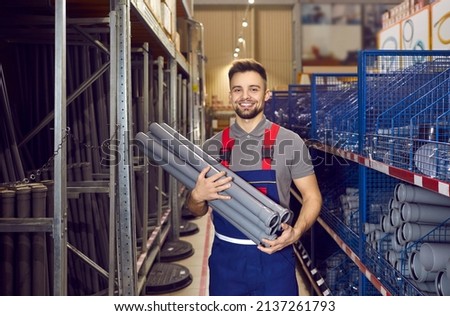 Happy young man who works as a salesman at the store where you can buy good quality tools and construction materials standing in one of the aisles and holding a bunch of gray PVC U drain pipes