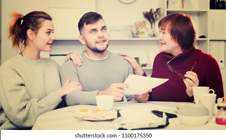 Happy Young Man With Wife And Mother Getting Good News, Reading Mail Together In Home Interior