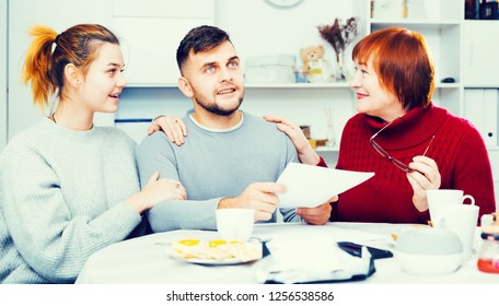 Happy Young Man With Wife And Mother Getting Good News, Reading Mail Together In Home Interior