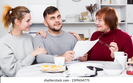 Happy Young Man With Wife And Mother Getting Good News, Reading Mail Together In Home Interior