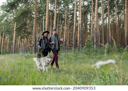 Happy young man and woman having chat while moving along footpath surrounded by pinetress in park or forest