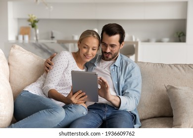 Happy young man and woman spouses relax on sofa in living room using modern tablet gadget together. Smiling Caucasian couple rest on couch at home talk on video call on pad. Technology concept. - Powered by Shutterstock