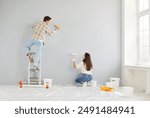 Happy young married couple enjoying wall painting, enjoy home renovation fun, decorate, repair after moving into new house, excited homeowners, renters, man and woman feeling joy, working together