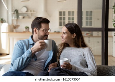 Happy young married couple enjoying cozy romantic weekend time with cup of hot tea coffee chocolate. Smiling pleasant family spouse relaxing on sofa, heart-to-hear talk, spending evening together. - Powered by Shutterstock