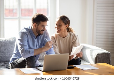 Happy young married couple sit on couch calculate expenses use easy online banking service at home, smiling millennial husband and wife count taxes house expenditures pay bills on internet - Shutterstock ID 1606546729