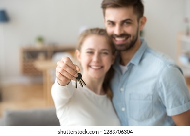 Happy young married family couple holding keys to new flat, excited home owners tenants looking at camera in own house, smiling customers buying estate modern apartment, property ownership concept
