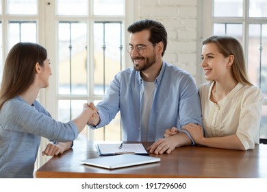 Happy young married family couple shaking hands with real estate agent, getting acquainted at meeting, celebrating making agreement or thanking for high quality professional service in office.