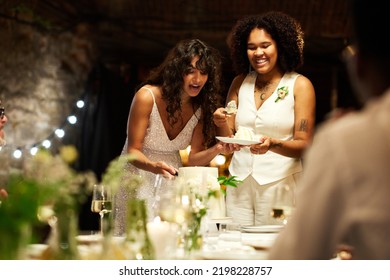 Happy young married lesbian couple in wedding apparel cutting big tasty cake for guests while standing in front of served festive table - Powered by Shutterstock