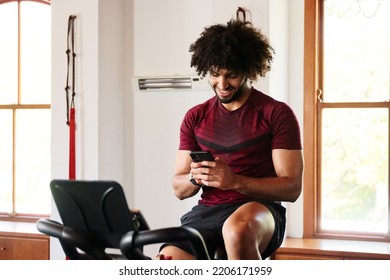 Happy Young Middle Eastern Man Using Mobile Phone On Exercise Bike At The Gym